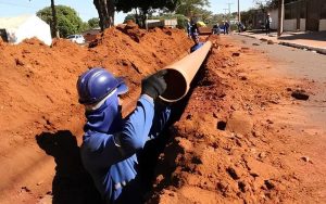 Trabalhador instala tubulação em obra de saneamento básico, reforçando a importância da infraestrutura para ampliar o acesso à água tratada e à coleta de esgoto no Brasil.